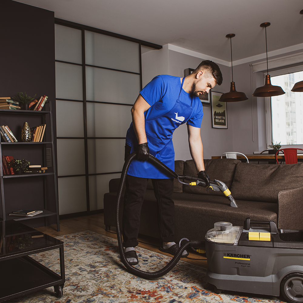 Pranie kanapy Kraków – pracownik firmy sprzątającej czyści sofę w salonie przy użyciu profesjonalnego odkurzacza piorącego.