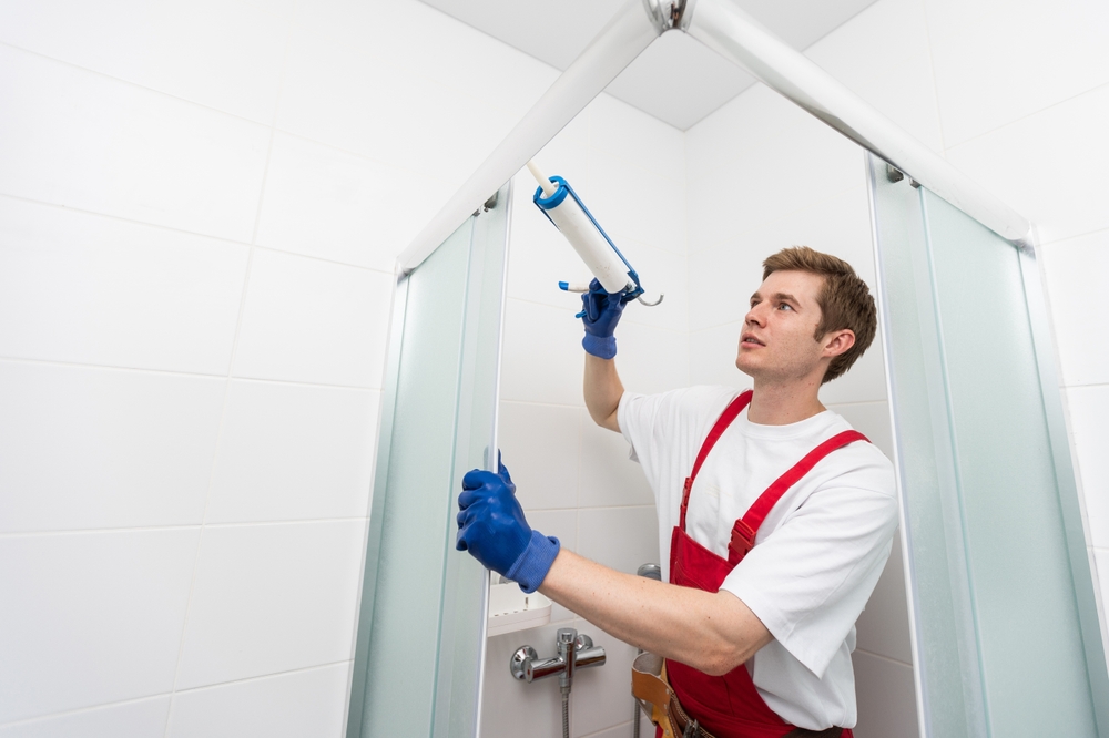 Budowniczy nakłada silikon w kabinie prysznicowej.