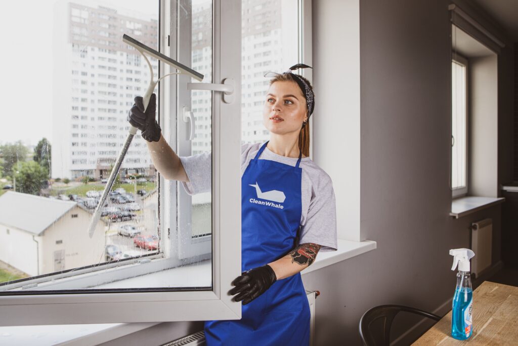 CleanWhale worker in a blue apron cleans a window with a mop in an apartment.