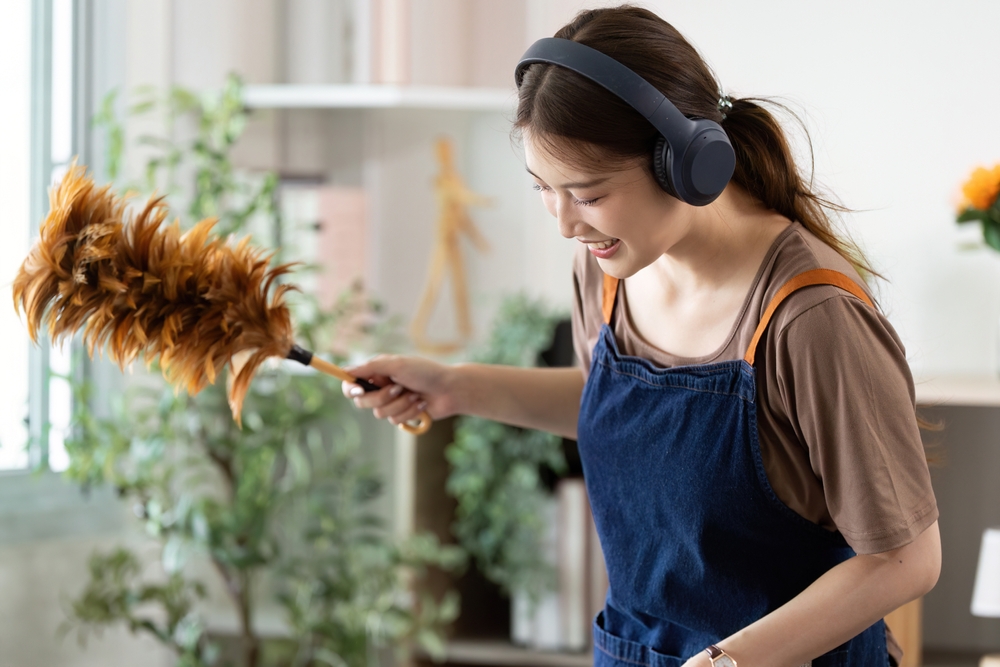 Жінка видаляє пил під час прибирання та слухає музику в навушниках.